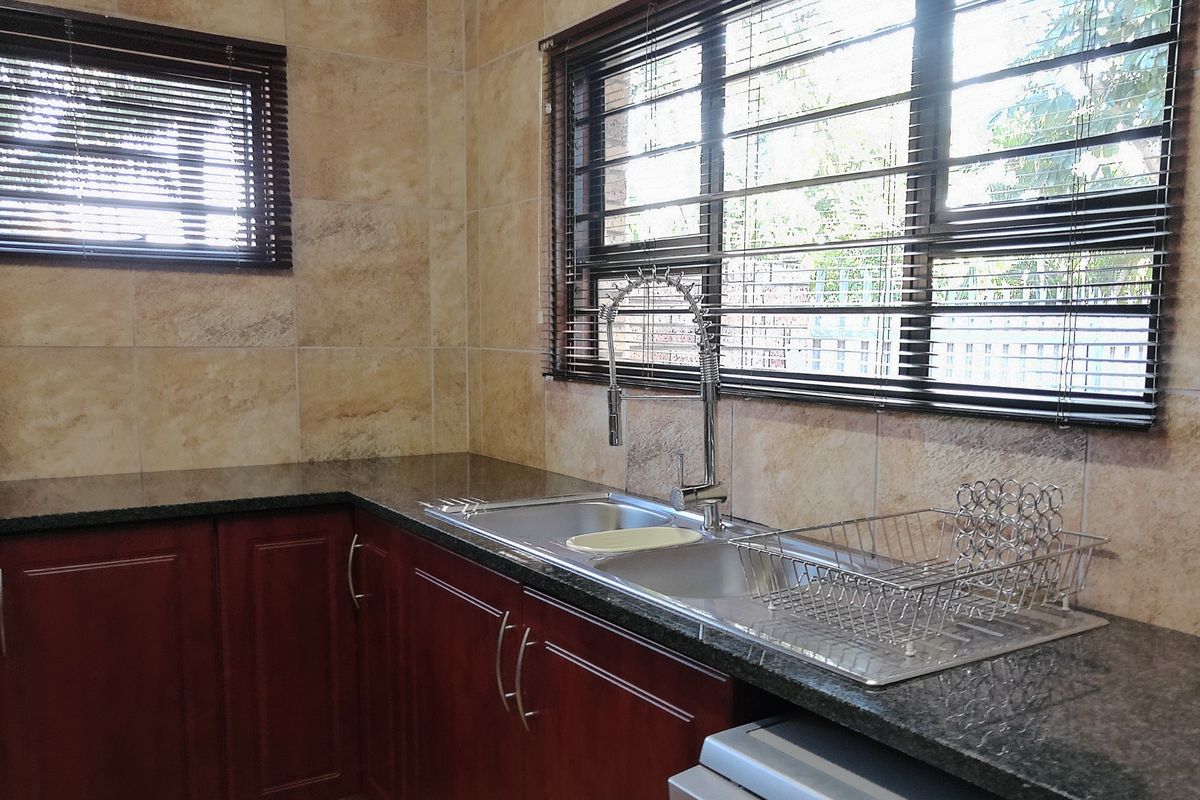 A functional kitchen area featuring dark wood cabinetry, granite countertops, a double stainless steel sink with a gooseneck faucet, and tiled wall finishes.