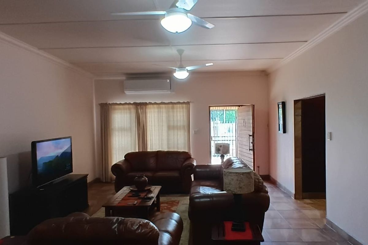 Spacious living room featuring tiled flooring, ceiling fans, and a wall-mounted air conditioning unit, providing a comfortable and functional living space.