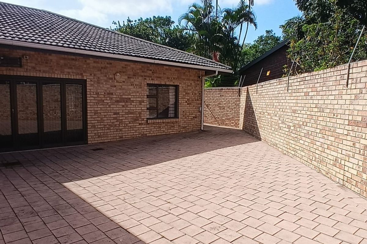 A paved rear courtyard area featuring face-brick exterior walls, dark-framed sliding doors, and a secure perimeter wall with electric fencing.