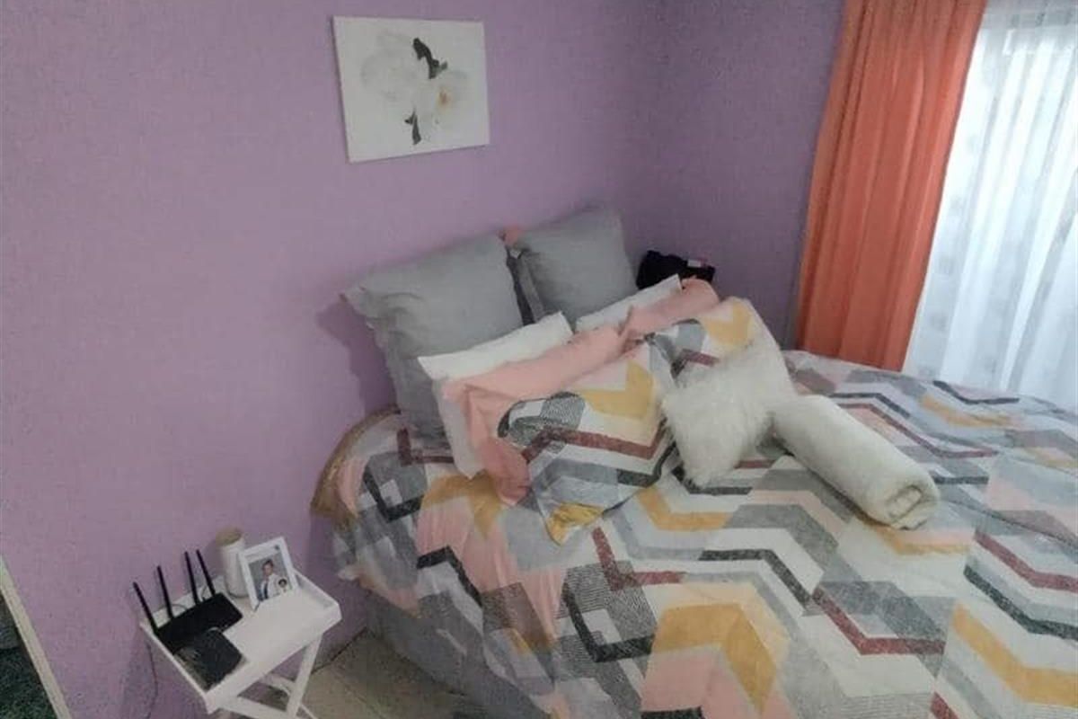 A bedroom featuring purple walls, crown molding, and tiled flooring, providing a functional space with natural light from the window.
