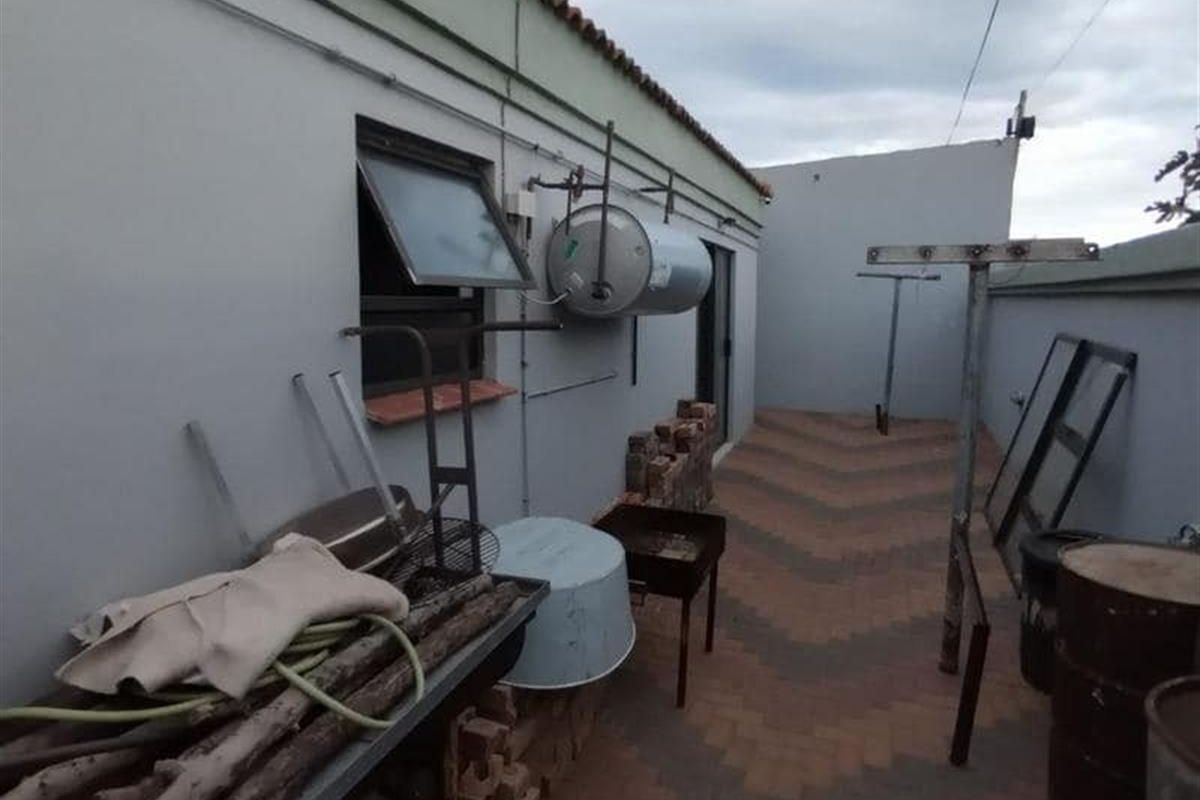 A functional exterior utility area featuring paved flooring, an external geyser, and a metal washing line, suitable for service and storage purposes.