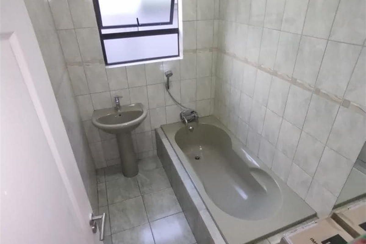 A compact bathroom featuring a built-in bathtub, pedestal basin, and tiled walls, offering a functional space ready for modernization.