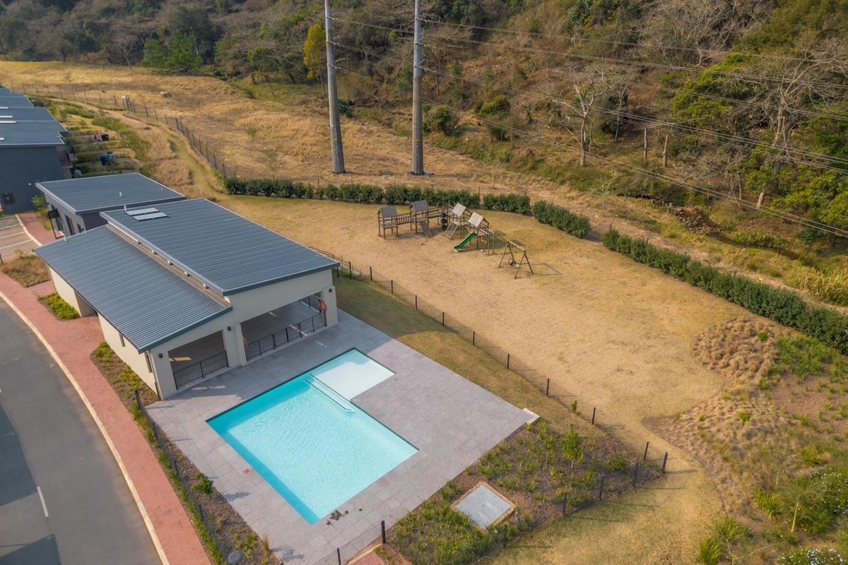 Aerial view of a residential complex featuring a swimming pool, covered patio area, and an adjacent playground set within a landscaped garden.