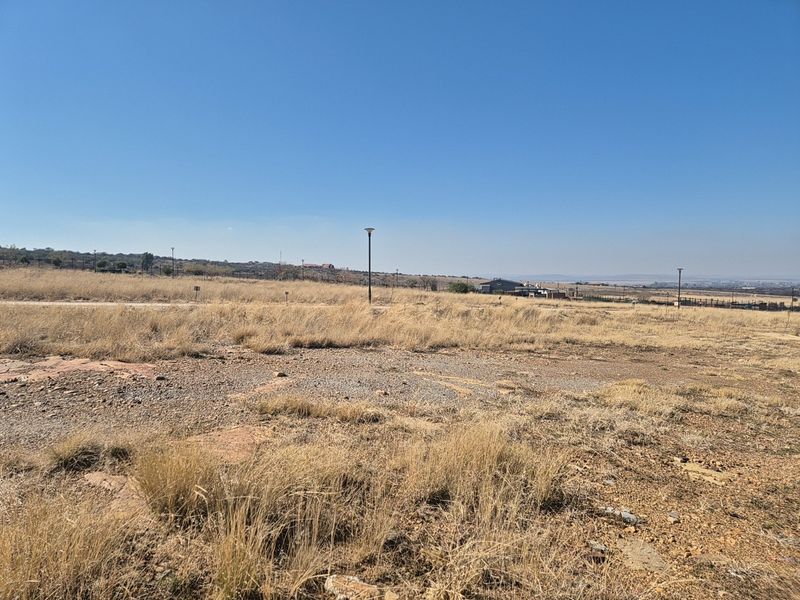 A vacant residential plot featuring dry grass and established street lighting, offering an open landscape with distant views.