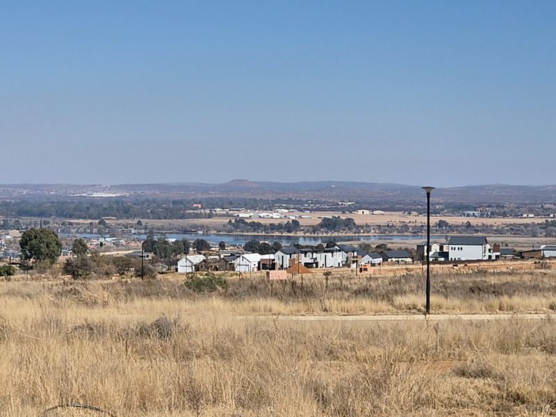 A wide-angle view of the surrounding landscape, featuring open fields, distant residential developments, and a scenic water body under a clear sky.