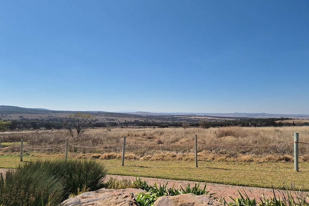 A scenic view of the surrounding landscape featuring a well-maintained garden, paved walkway, and post and rope fencing.
