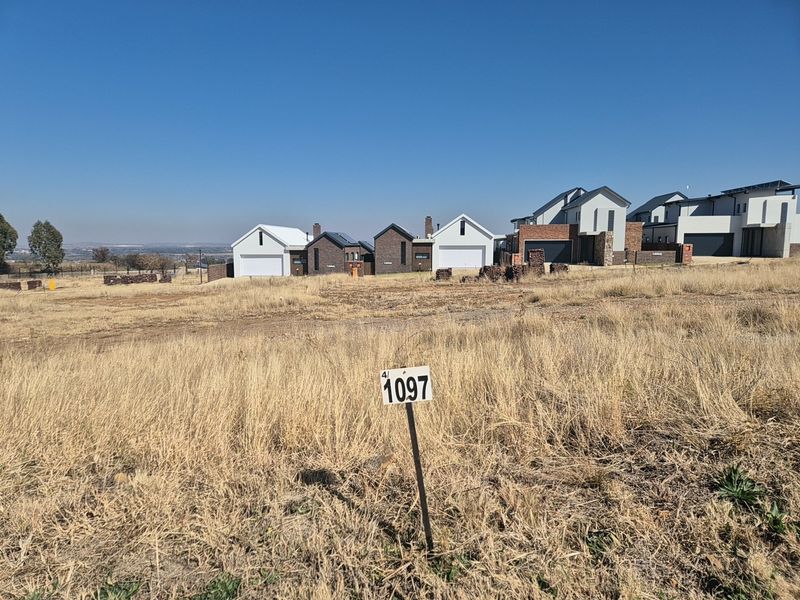 A vacant residential plot of land featuring a boundary marker, situated in a developed estate with surrounding modern homes.