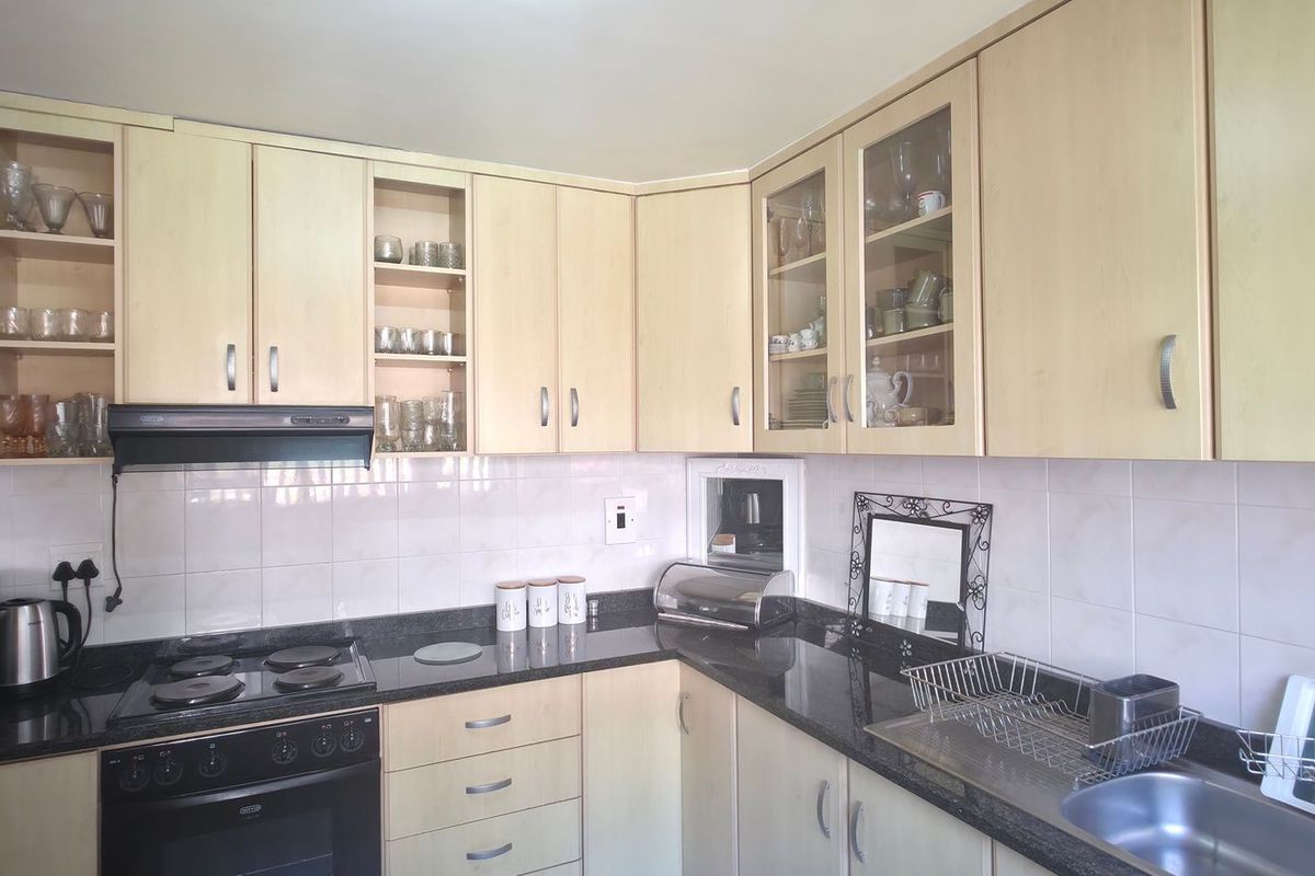 A functional kitchen featuring light wood-tone cabinetry, dark granite countertops, a tiled backsplash, and integrated cooking appliances.