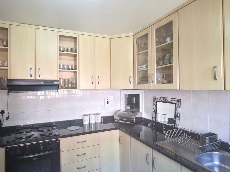 A functional kitchen featuring light wood-tone cabinetry, dark granite countertops, a tiled backsplash, and integrated cooking appliances.