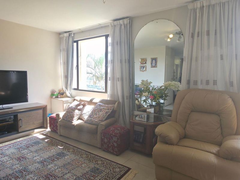 A bright living room featuring tiled flooring, large windows with natural light, and a prominent wall-mounted mirror.