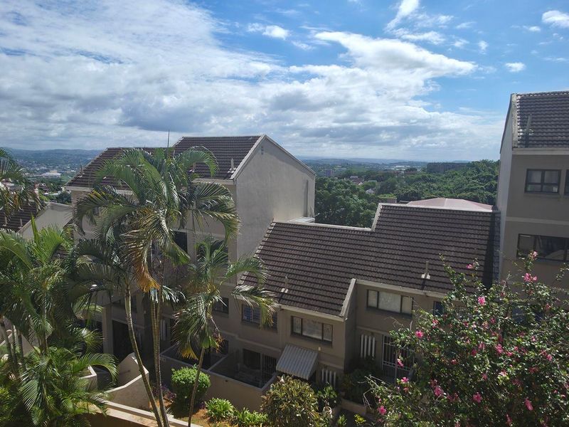 Elevated view overlooking the surrounding residential estate, featuring tiled roof architecture and lush greenery under a clear sky.