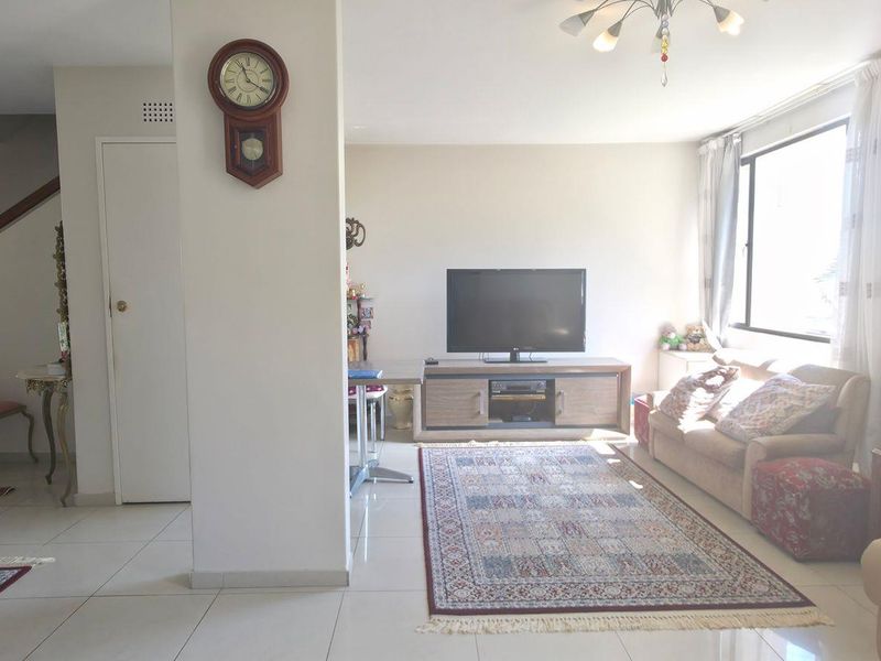 A spacious living area featuring tiled flooring, a staircase, and large windows that provide ample natural light to the open-plan space.