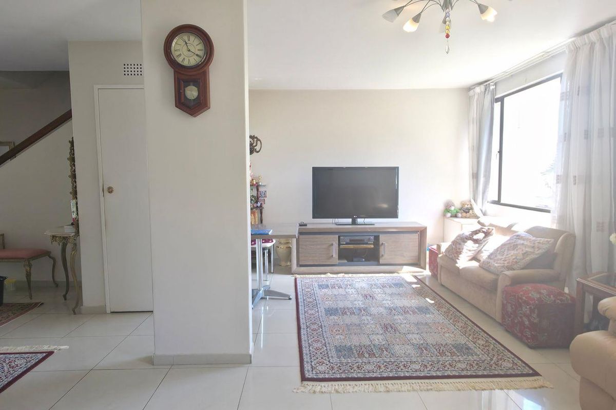 A spacious living area featuring tiled flooring, a staircase, and large windows that provide ample natural light to the open-plan space.