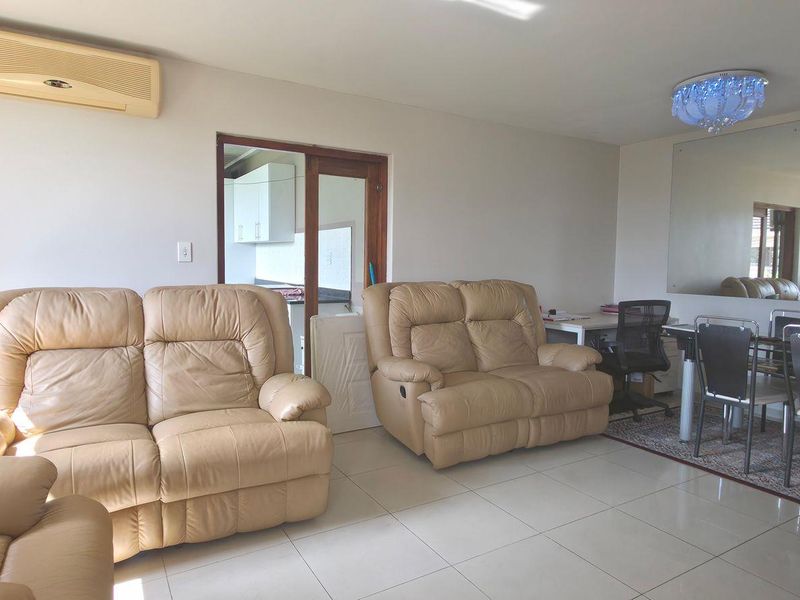 A spacious living area featuring tiled flooring, a wall-mounted air conditioning unit, and a large feature mirror, with direct access to the kitchen area.