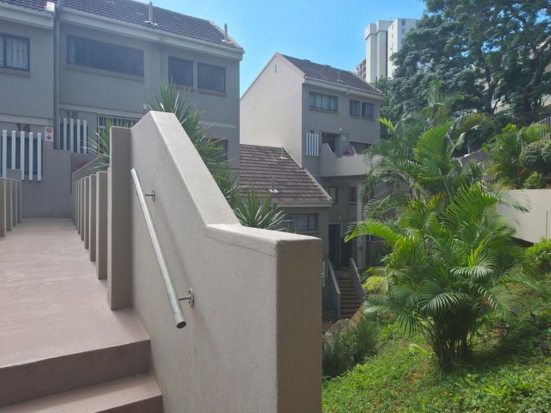 A view of the exterior rear area featuring a concrete staircase with a metal handrail, leading towards the residential units and landscaped garden.