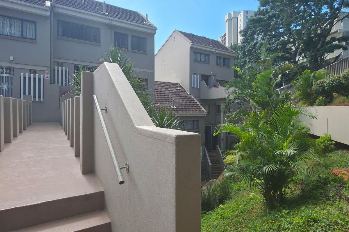 A view of the exterior rear area featuring a concrete staircase with a metal handrail, leading towards the residential units and landscaped garden.