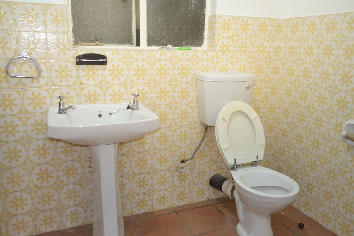 A dated bathroom featuring a pedestal basin and a standard toilet with exposed plumbing, finished with vintage patterned wall tiles.