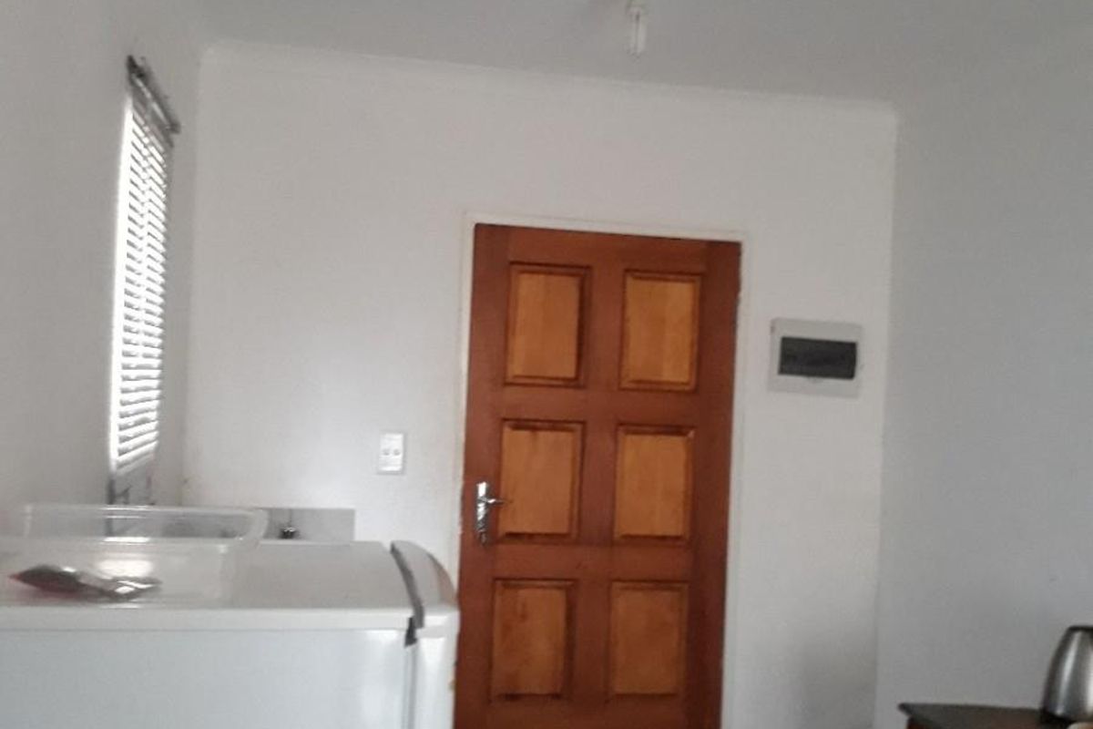 A functional kitchen area featuring tiled flooring, a solid wooden door, and a window fitted with venetian blinds.