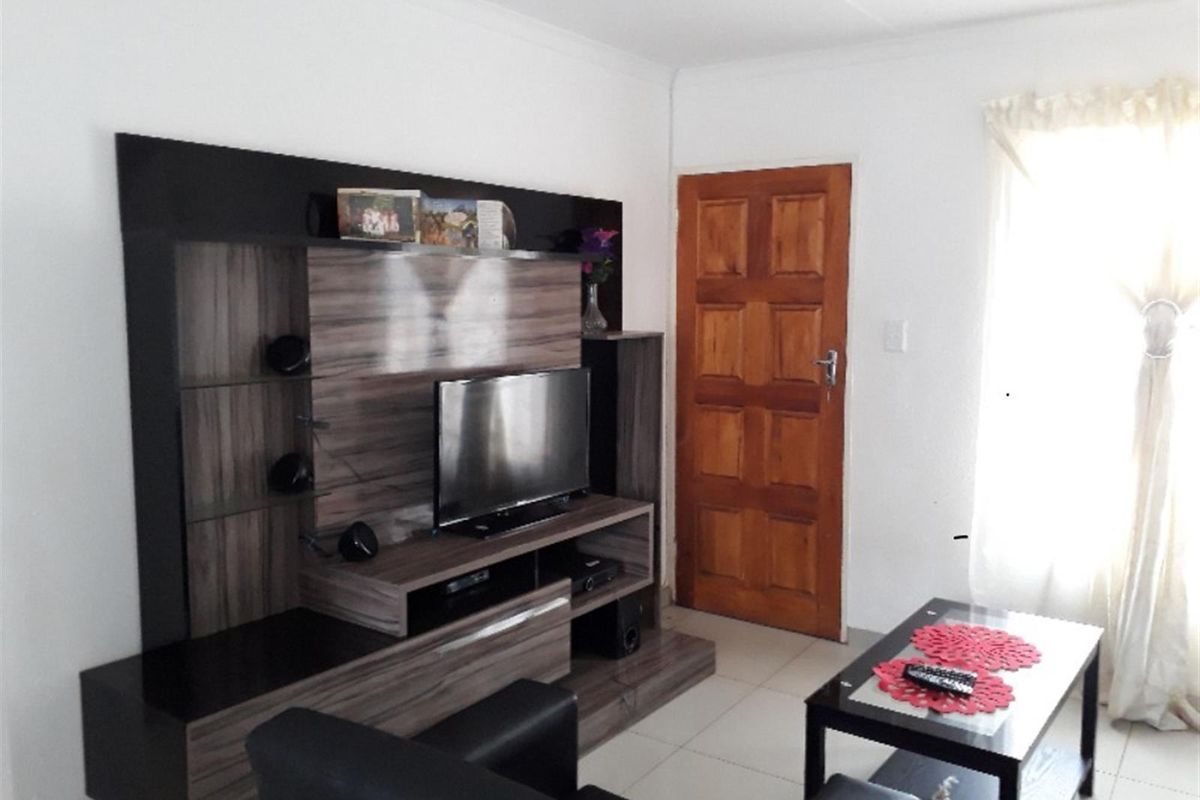 A living room featuring tiled flooring and a solid timber door, providing a functional and neutral space for relaxation.