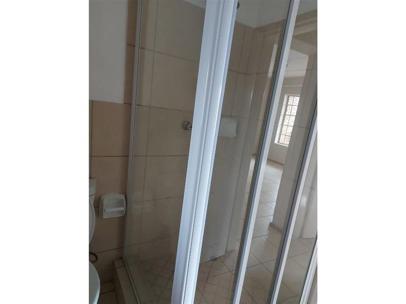 A functional bathroom featuring a glass shower enclosure, tiled walls, and tiled flooring, presenting a clean and neutral space.