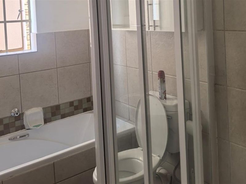 A functional bathroom featuring a bathtub, a separate shower enclosure, and a toilet, finished with neutral wall tiling.