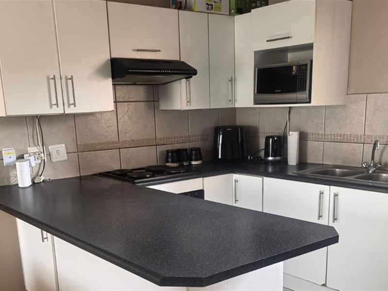 A functional kitchen featuring white cabinetry, dark laminate countertops, a tiled backsplash, and integrated appliances including a hob and extractor fan.