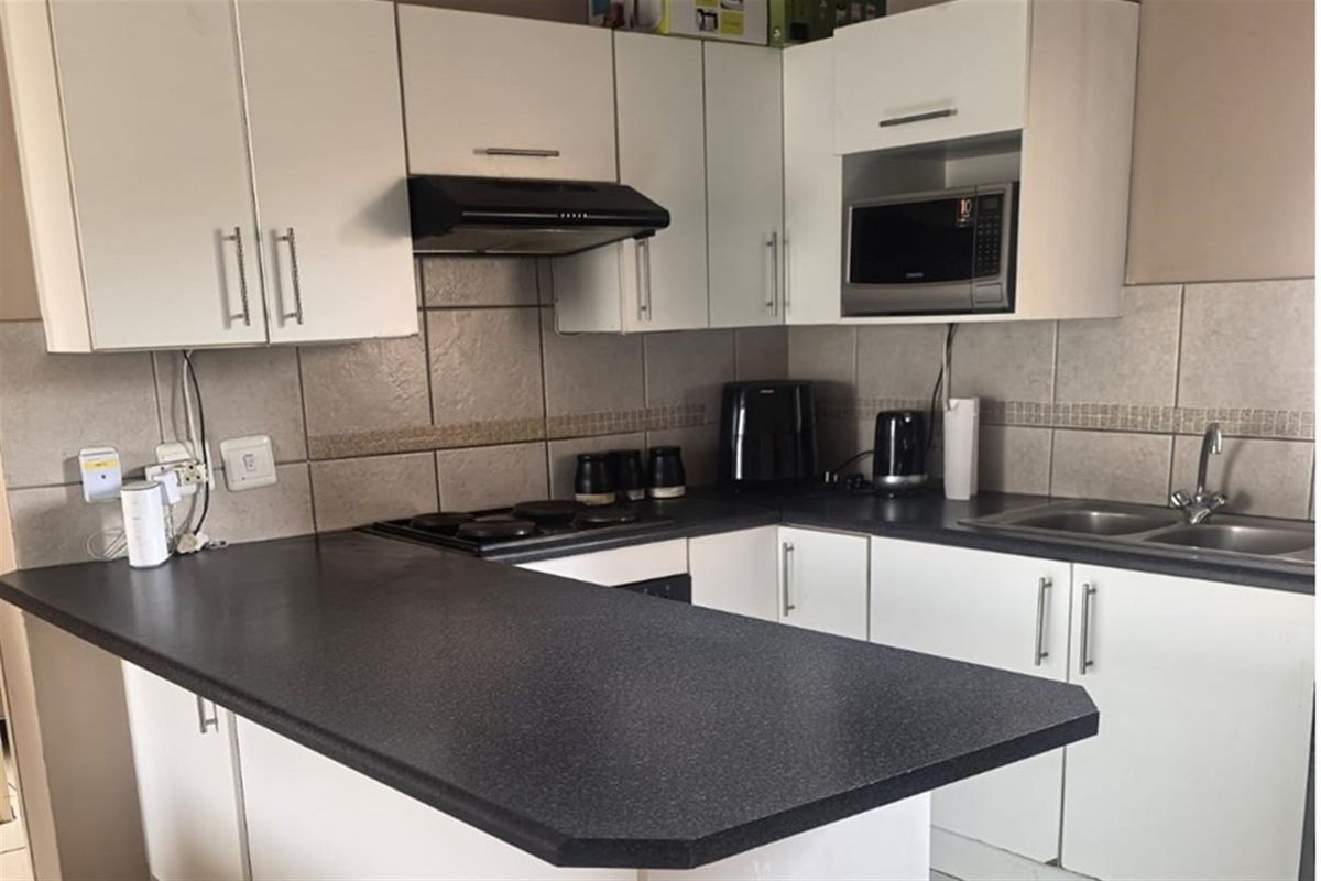 A functional kitchen featuring white cabinetry, dark laminate countertops, a tiled backsplash, and integrated appliances including a hob and extractor fan.