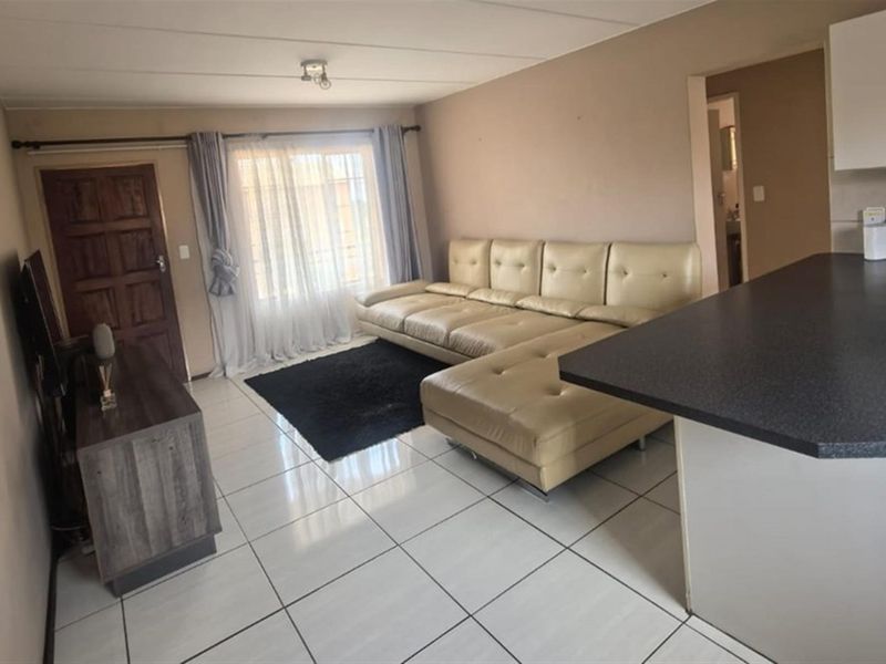 Open-plan living area featuring tiled flooring, a kitchen breakfast bar with cabinetry, and direct access to the main entrance.