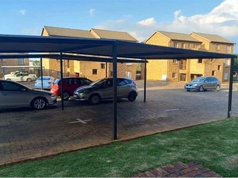 A paved parking area featuring a covered carport structure situated in front of a brick townhouse complex.