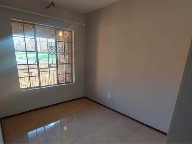 A vacant bedroom featuring neutral wall paint, tiled flooring, and a window fitted with security bars.