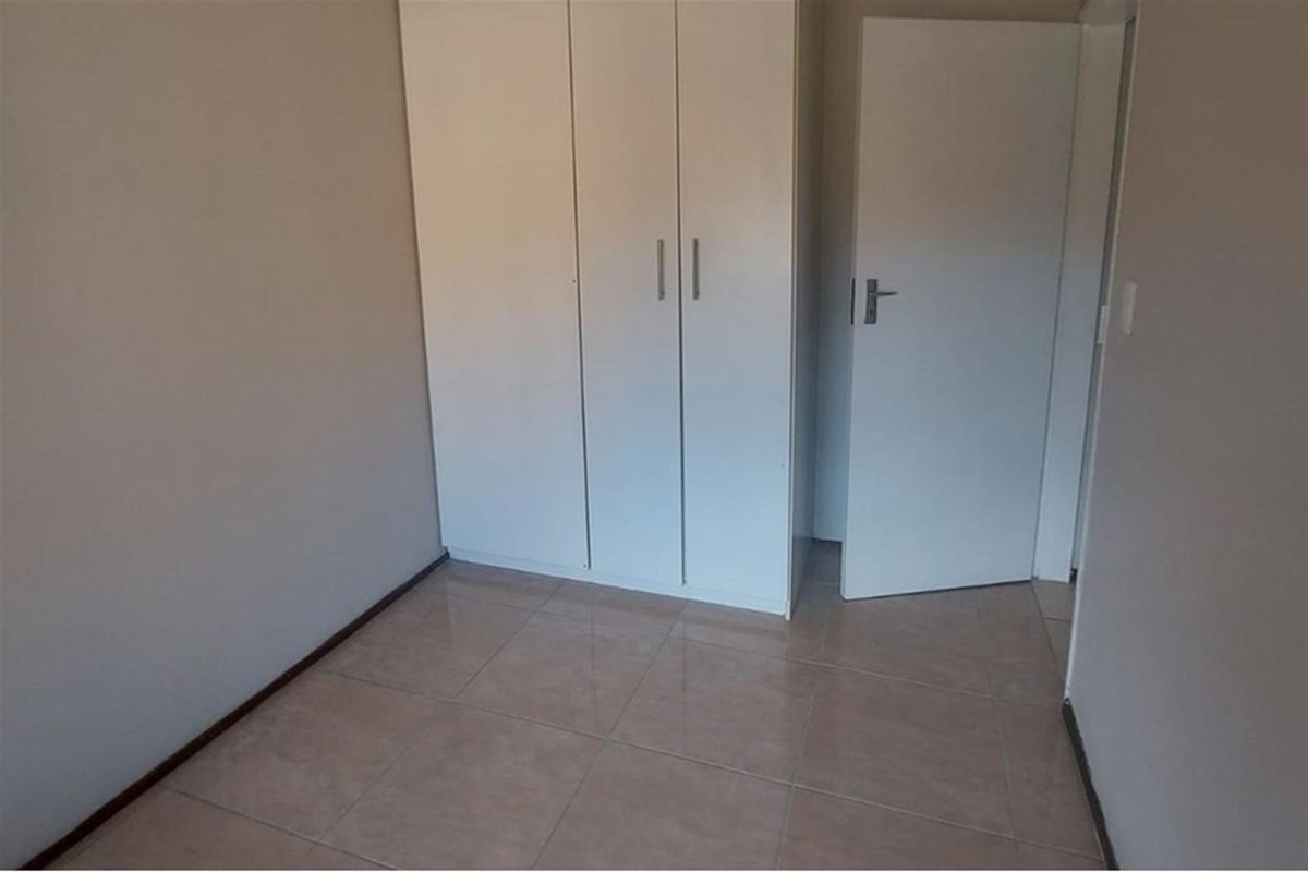 A clean, empty bedroom featuring neutral tiled flooring and white built-in cupboards, offering a blank canvas for personalization.