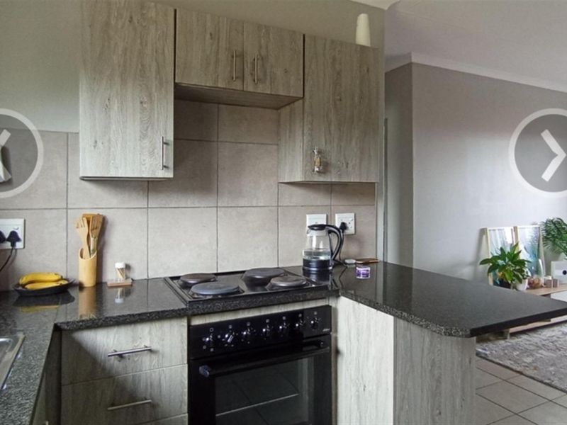 A compact kitchen featuring wood-look cabinetry, granite countertops, a built-in oven with a hob, and tiled splashbacks, seamlessly flowing into the adjacent living area.
