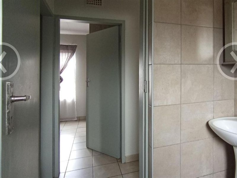 A view from a tiled bathroom looking through a doorway into an adjacent bedroom, featuring neutral wall tones and standard interior door fixtures.