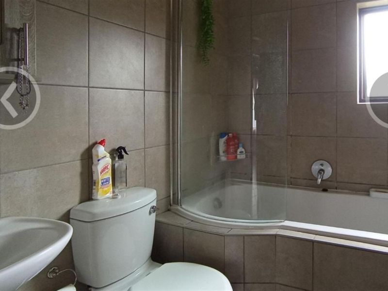 A functional bathroom featuring a tiled bathtub with a glass shower screen, a pedestal basin, and a standard toilet.