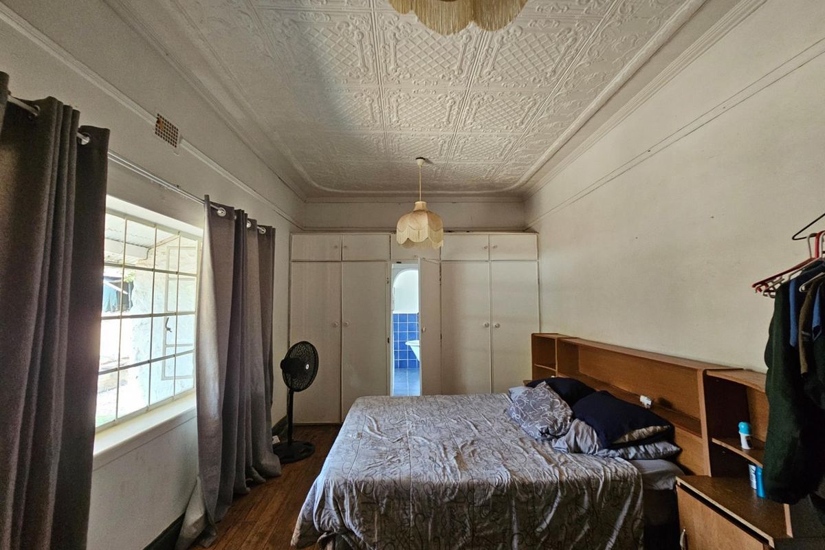 A bedroom featuring original pressed metal ceilings, built-in cabinetry, and timber flooring, with an adjoining bathroom visible through the central door.