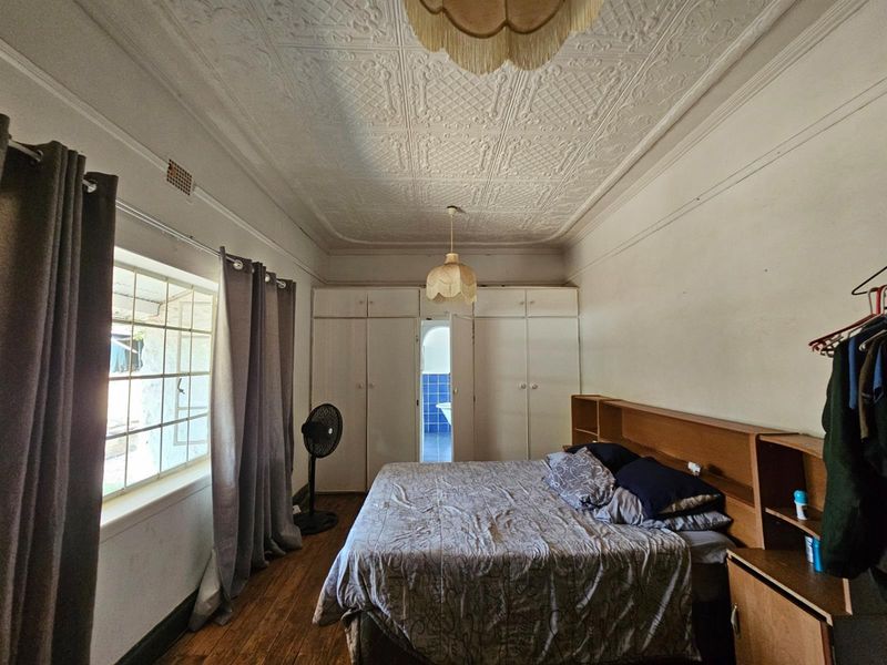 A bedroom featuring original pressed metal ceilings, built-in cabinetry, and timber flooring, with an adjoining bathroom visible through the central door.