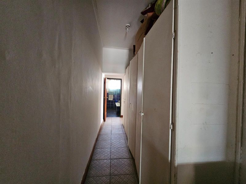 A narrow hallway featuring built-in storage cupboards along one side, leading towards a bathroom at the end of the corridor.