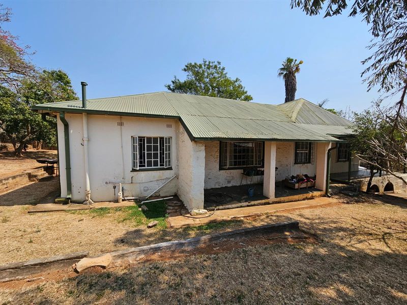 Rear view of a single-story house featuring a corrugated metal roof, covered patio area, and masonry walls requiring maintenance and exterior restoration.