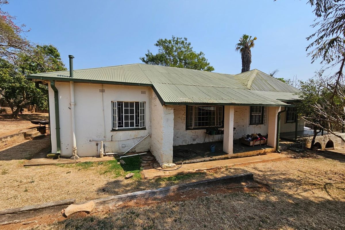 Rear view of a single-story house featuring a corrugated metal roof, covered patio area, and masonry walls requiring maintenance and exterior restoration.