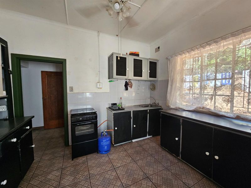 A dated kitchen featuring dark cabinetry, tiled flooring, and a freestanding stove, offering a functional space with potential for modernization.