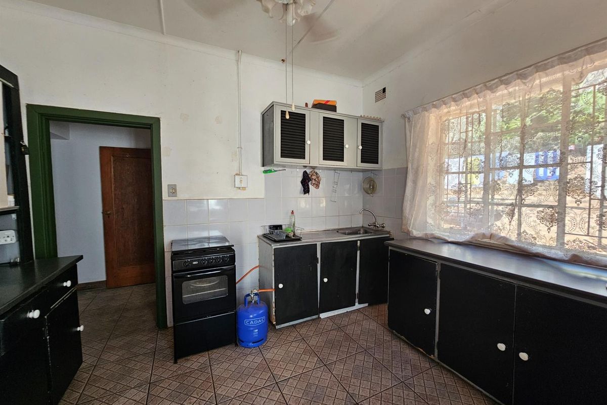 A dated kitchen featuring dark cabinetry, tiled flooring, and a freestanding stove, offering a functional space with potential for modernization.