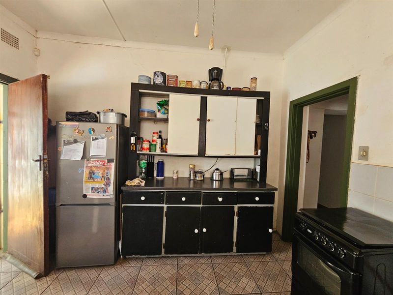 A functional kitchen area featuring built-in cabinetry, tiled flooring, and access to adjacent rooms, offering potential for modernization and cosmetic updates.