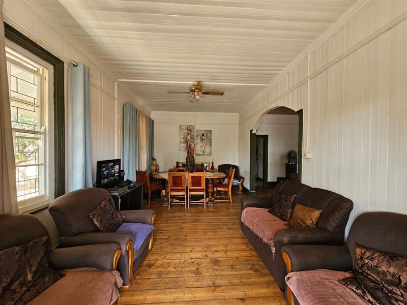 Open plan living and dining area featuring traditional timber wall paneling, exposed timber flooring, and a ceiling fan.