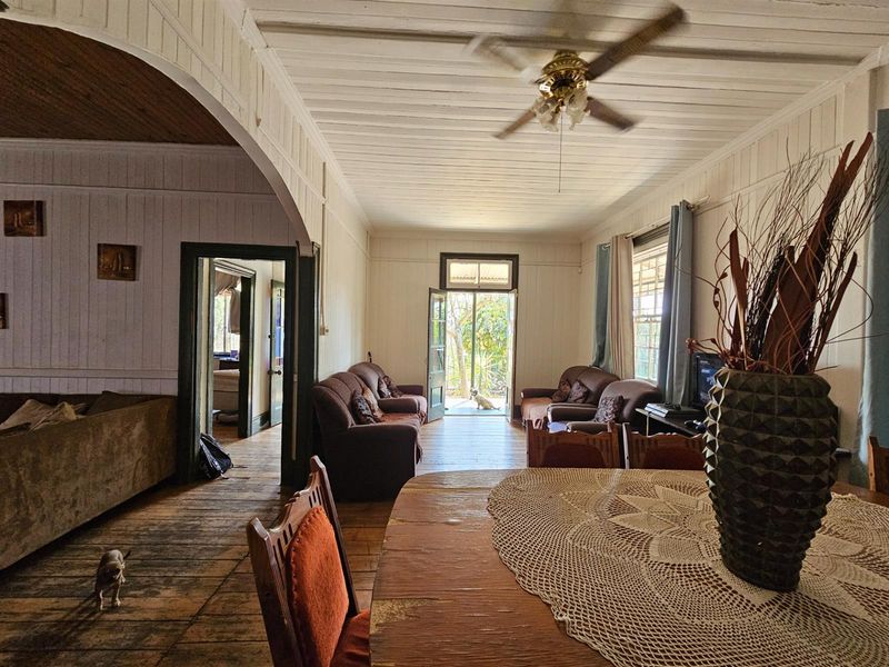 Spacious open-plan living and dining area featuring traditional timber wall paneling, exposed timber flooring, and a ceiling fan, with direct access to the garden.