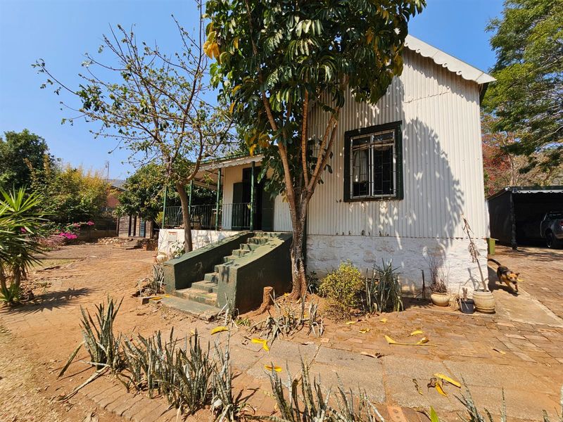 Exterior view of a cottage-style house featuring corrugated iron cladding, a raised front porch with steps, and surrounding garden area.