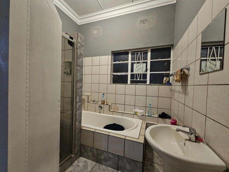 A functional bathroom featuring a built-in bathtub, separate shower enclosure, pedestal basin, and tiled wall finishes.