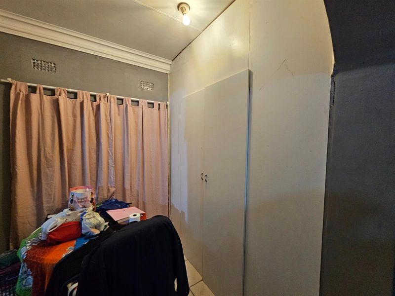 A bedroom featuring built-in cupboards, crown molding, and tiled flooring, currently showing signs of wear on the wall surfaces.