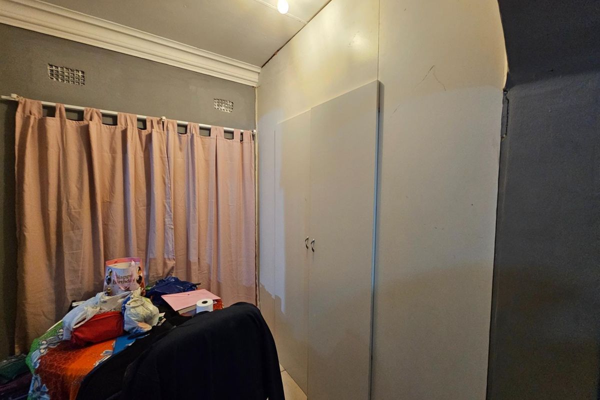 A bedroom featuring built-in cupboards, crown molding, and tiled flooring, currently showing signs of wear on the wall surfaces.