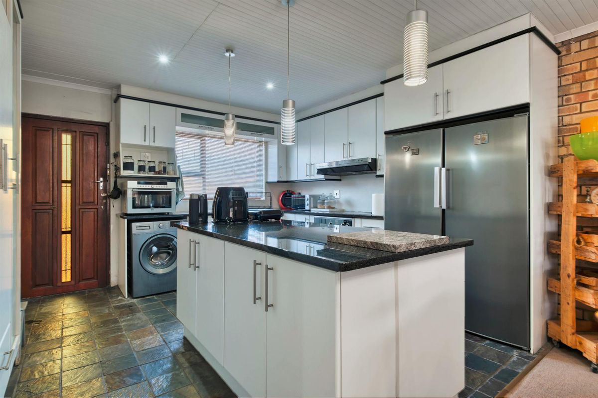 A functional kitchen featuring white cabinetry, a central island with granite countertops, integrated appliances, and slate-style floor tiling.