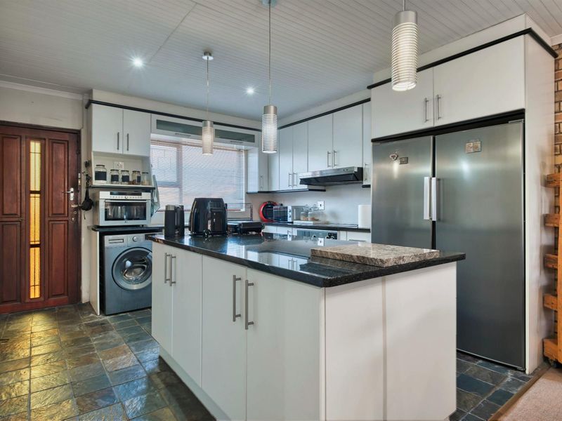 A functional kitchen featuring white cabinetry, a central island with granite countertops, integrated appliances, and slate-style floor tiling.
